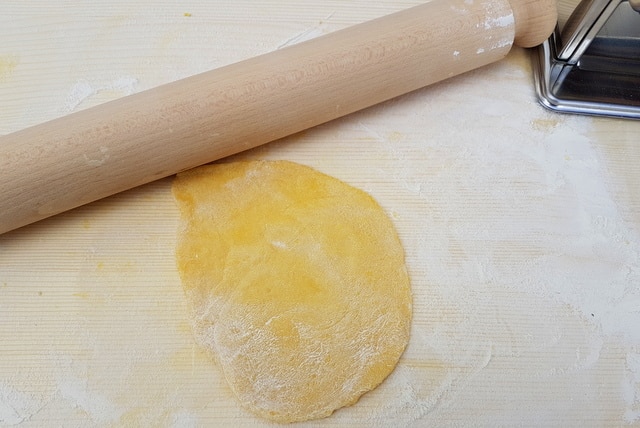 Rolled out homemade lasagne pasta dough on wooden board with rolling pin