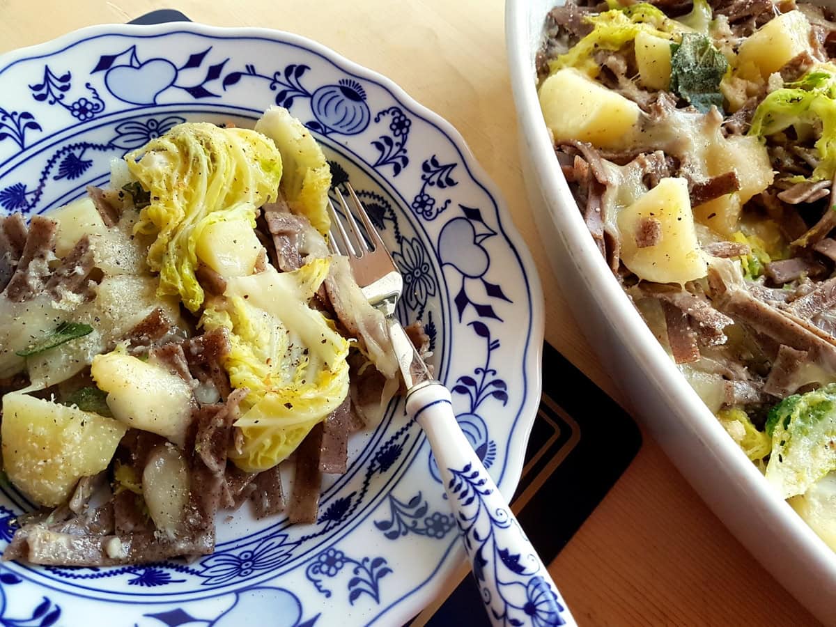 Baked pizzoccheri alla Valtellinese in blue and white plate.