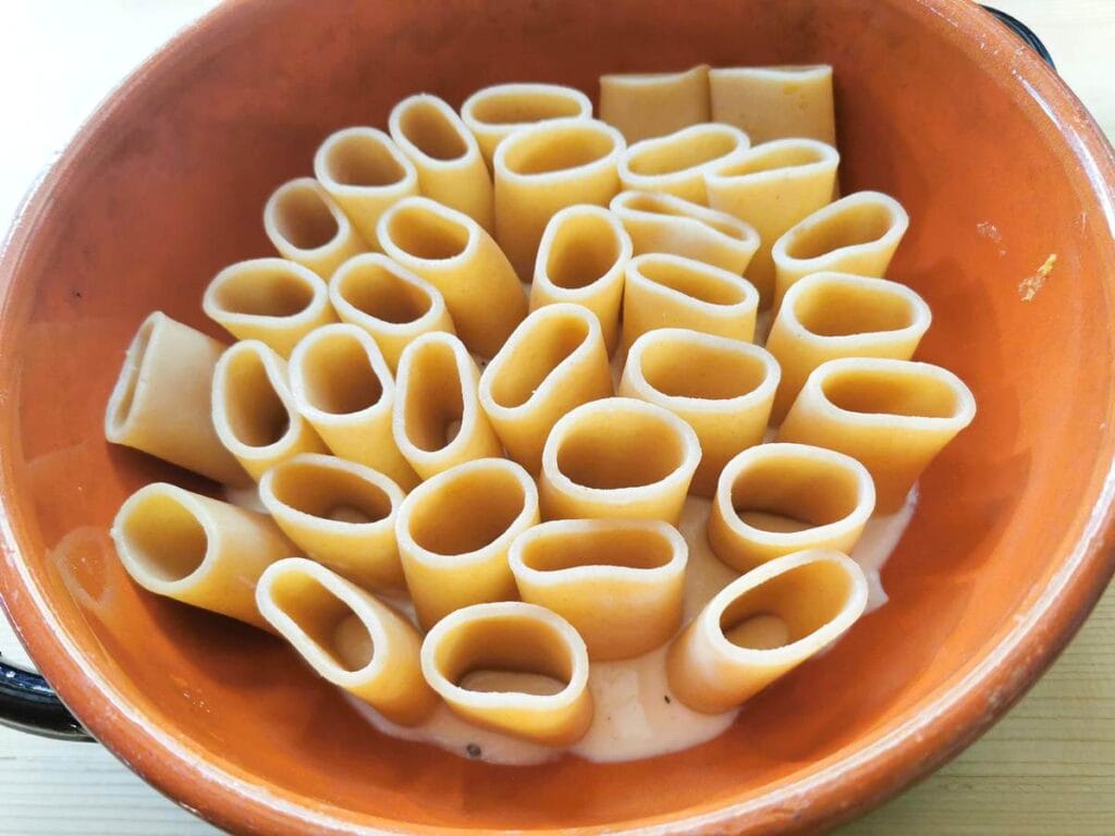 partly cooked paccheri tubes standing up in terracotta oven dish