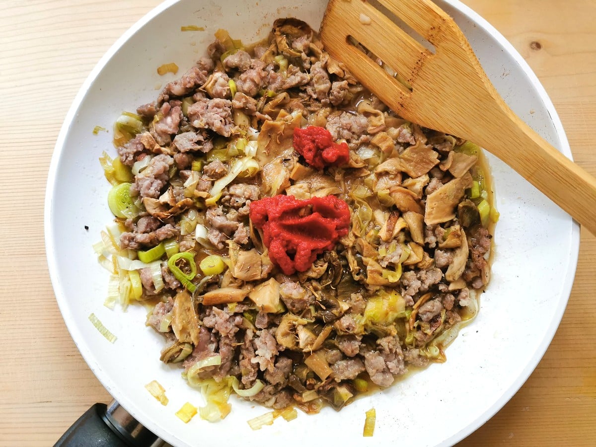 tomato concentrate added to sausage, leeks and mushrooms in frying pan