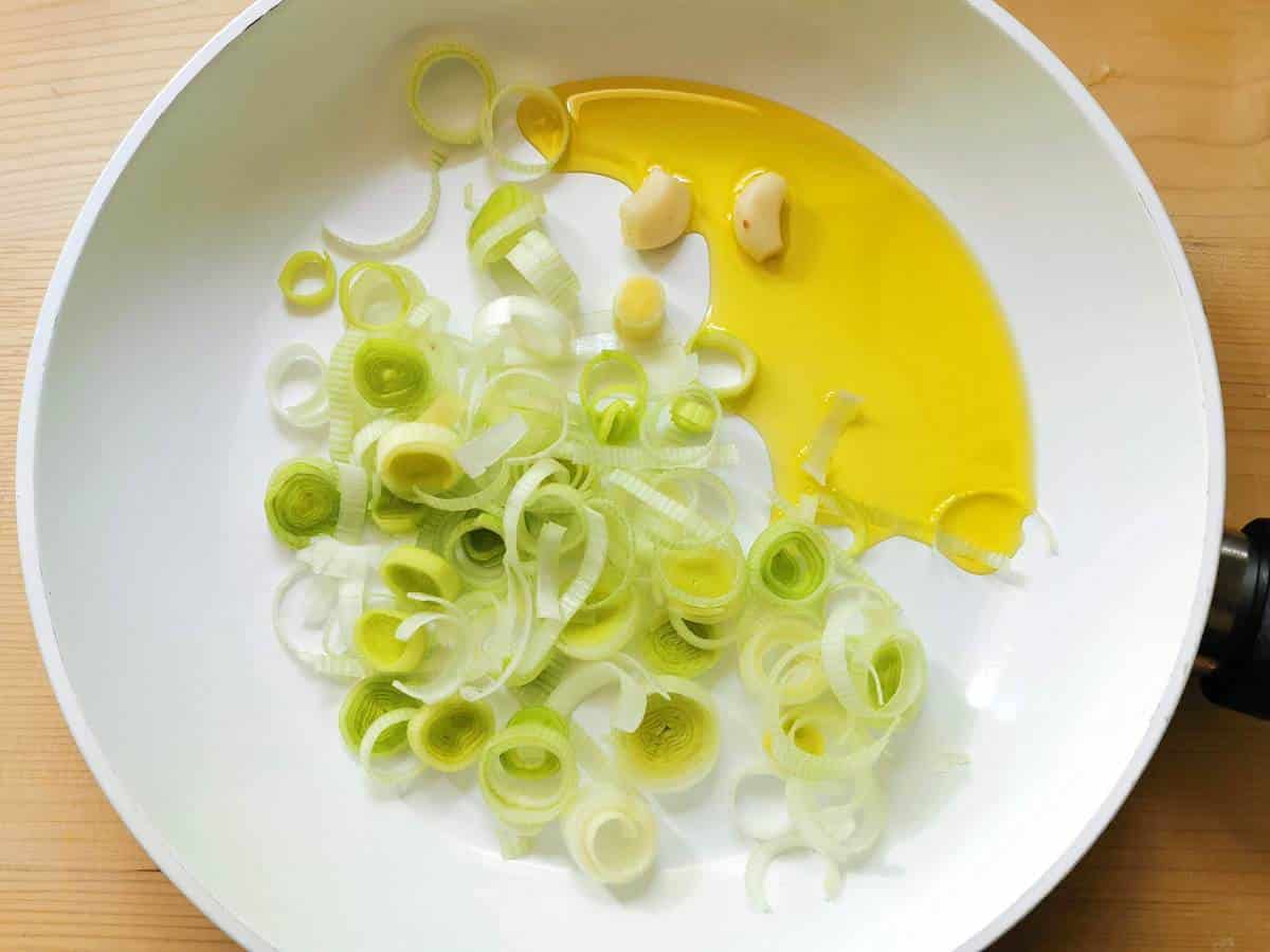 garlic clove and sliced leek in frying pan with olive oil