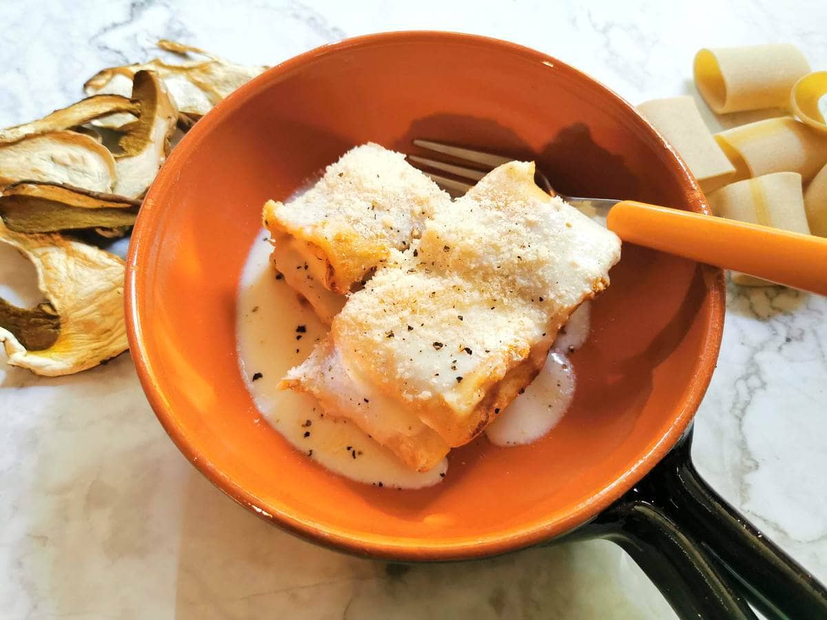 3 pieces of baked stuffed paccheri with sausage and mushrooms in a round terracotta bowl with a fork.