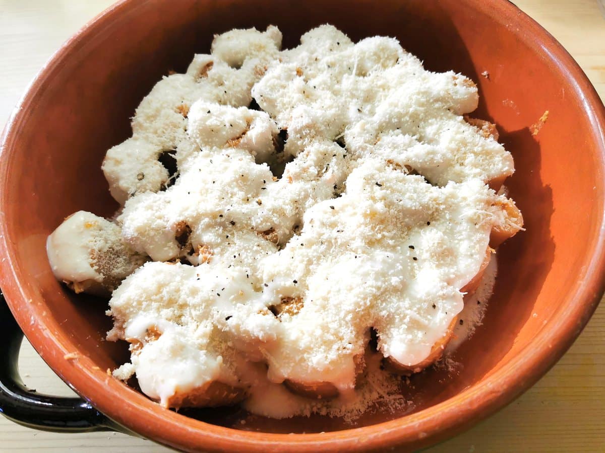 filled paccheri cover with béchamel and grated parmigiano in round terracotta oven dish