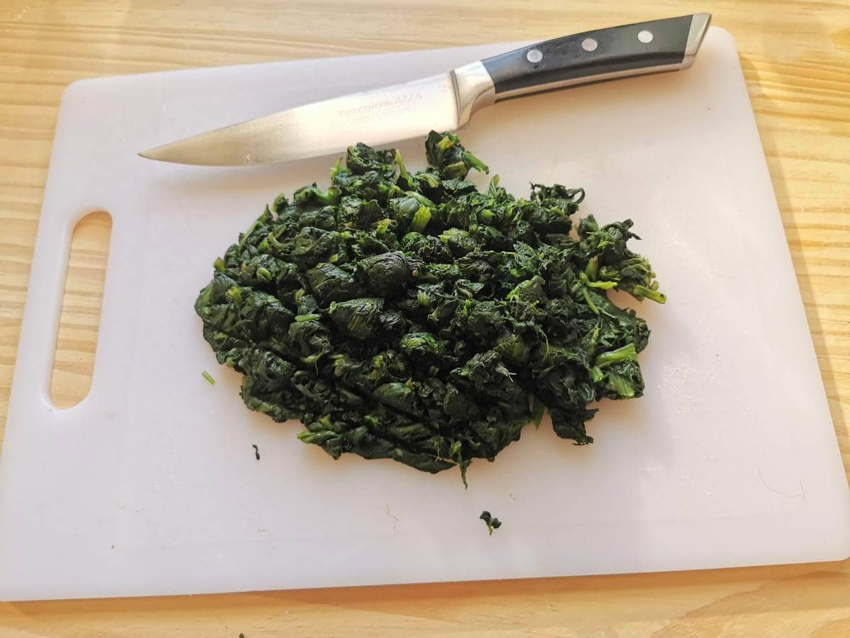 Chopped cooked spinach on white chopping board.