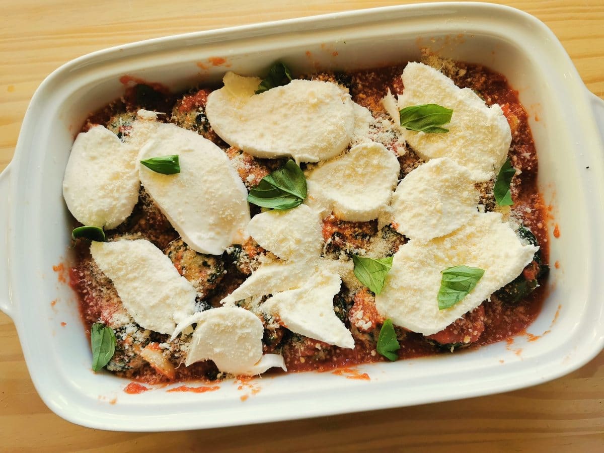 Gnudi in tomato sauce in an oven dish with a layer of mozzarella on top ready to go in the oven.