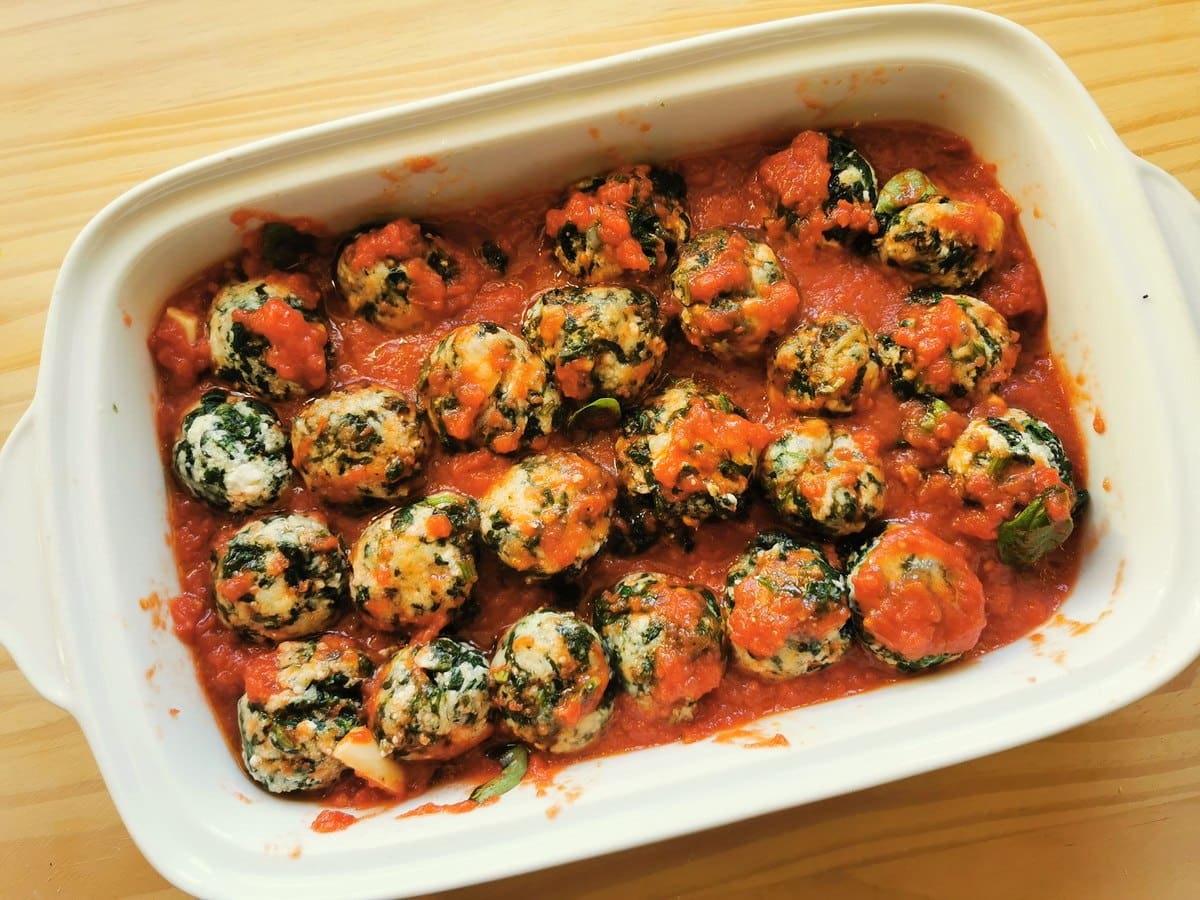 Boiled gnudi in white rectangular oven dish with tomato sauce.