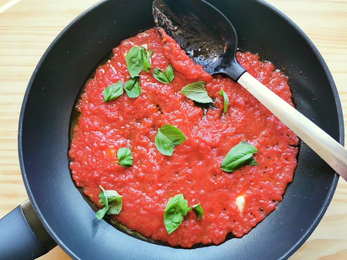 Ready tomato sauce with basil leaves in skillet.