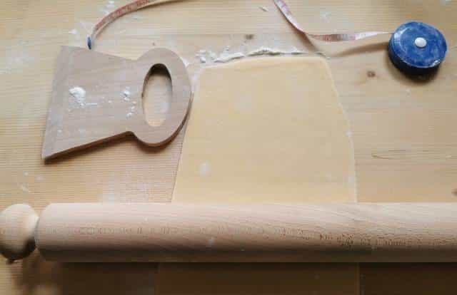 rolled out pasta sheet on pastry board with rolling pin, pasta cutter and measuring tape