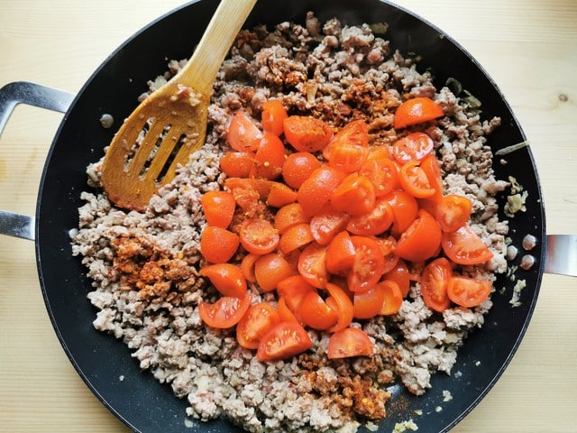 small tomatoes and red chili flakes added to meat and onions in skillet