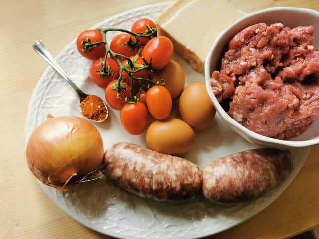 ingredients for beef and sausage ragu on white plate.