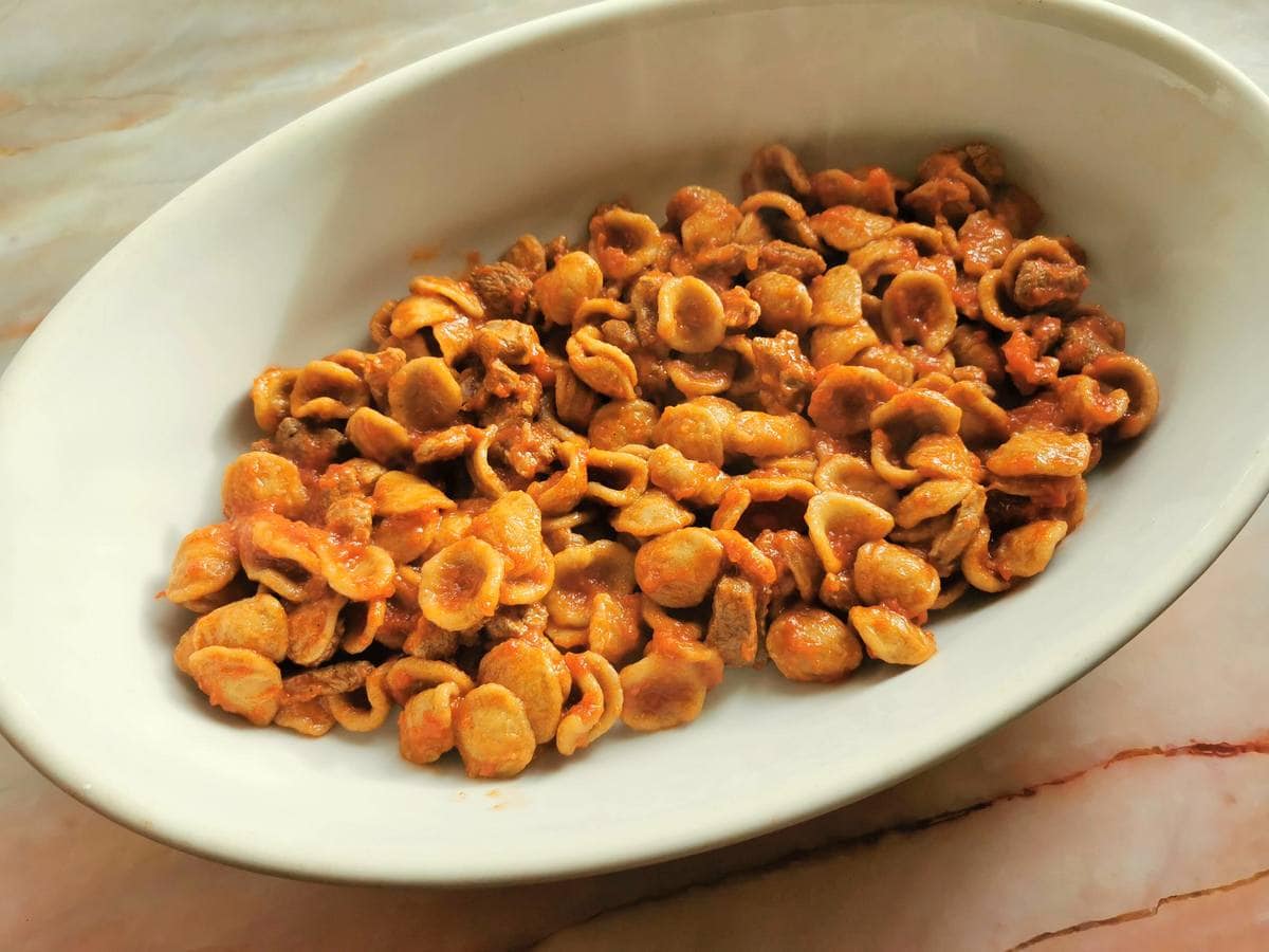 A layer of orecchiette with lamb sauce in oval oven dish.