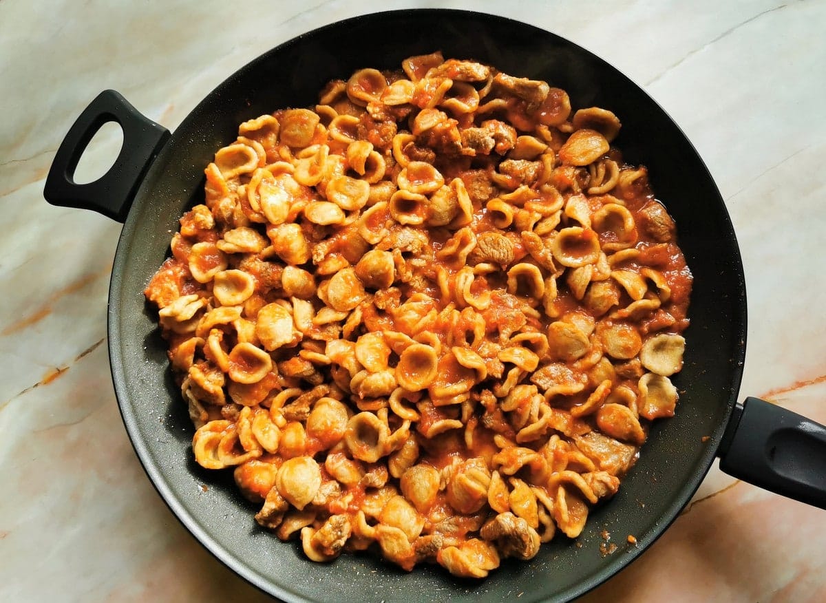 Cooked burnt wheat orecchiette mixed with lamb sauce in skillet.