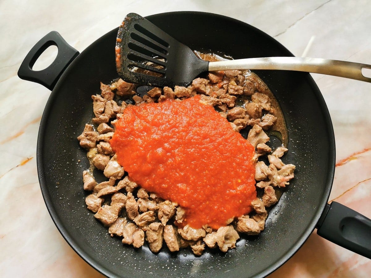 Tomato passata in skillet with browned lamb.