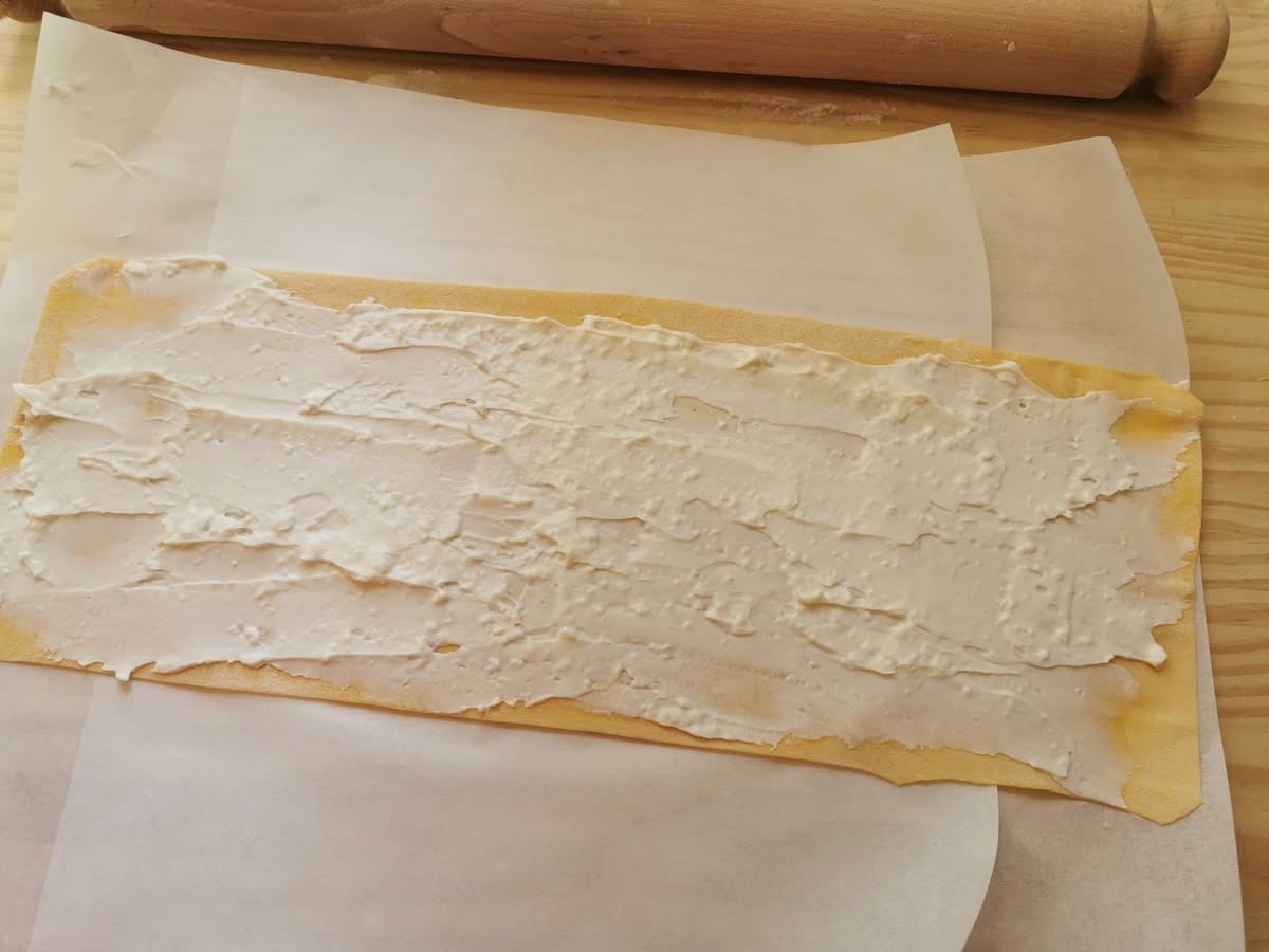 Sheet of homemade pasta with stracchino cheese spread over it.