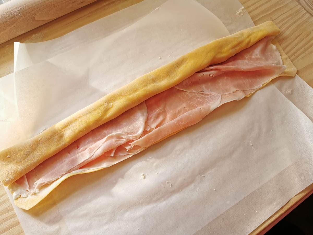 Fresh pasta sheet being rolled with ham and cheese in the middle.