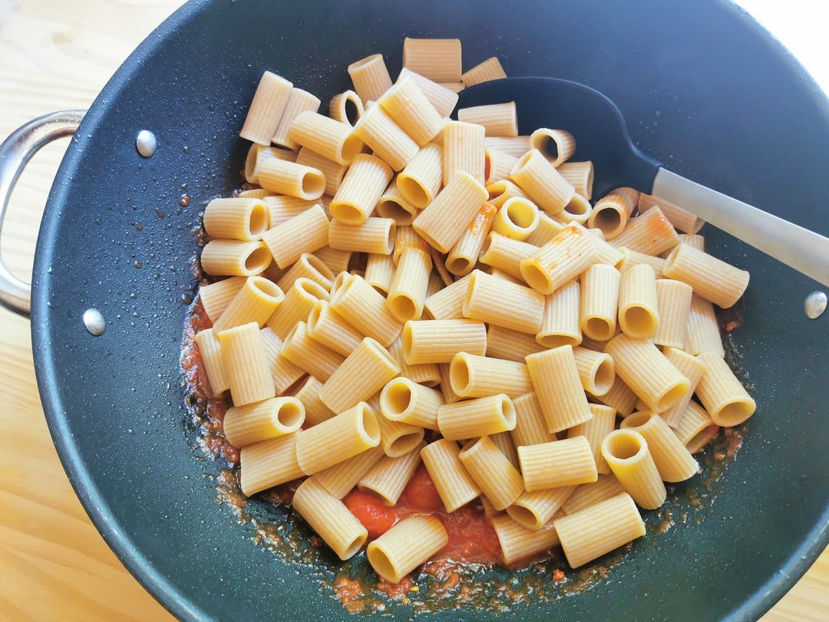 Cooked whole wheat pasta tubes added to tomato sauce in large skillet.