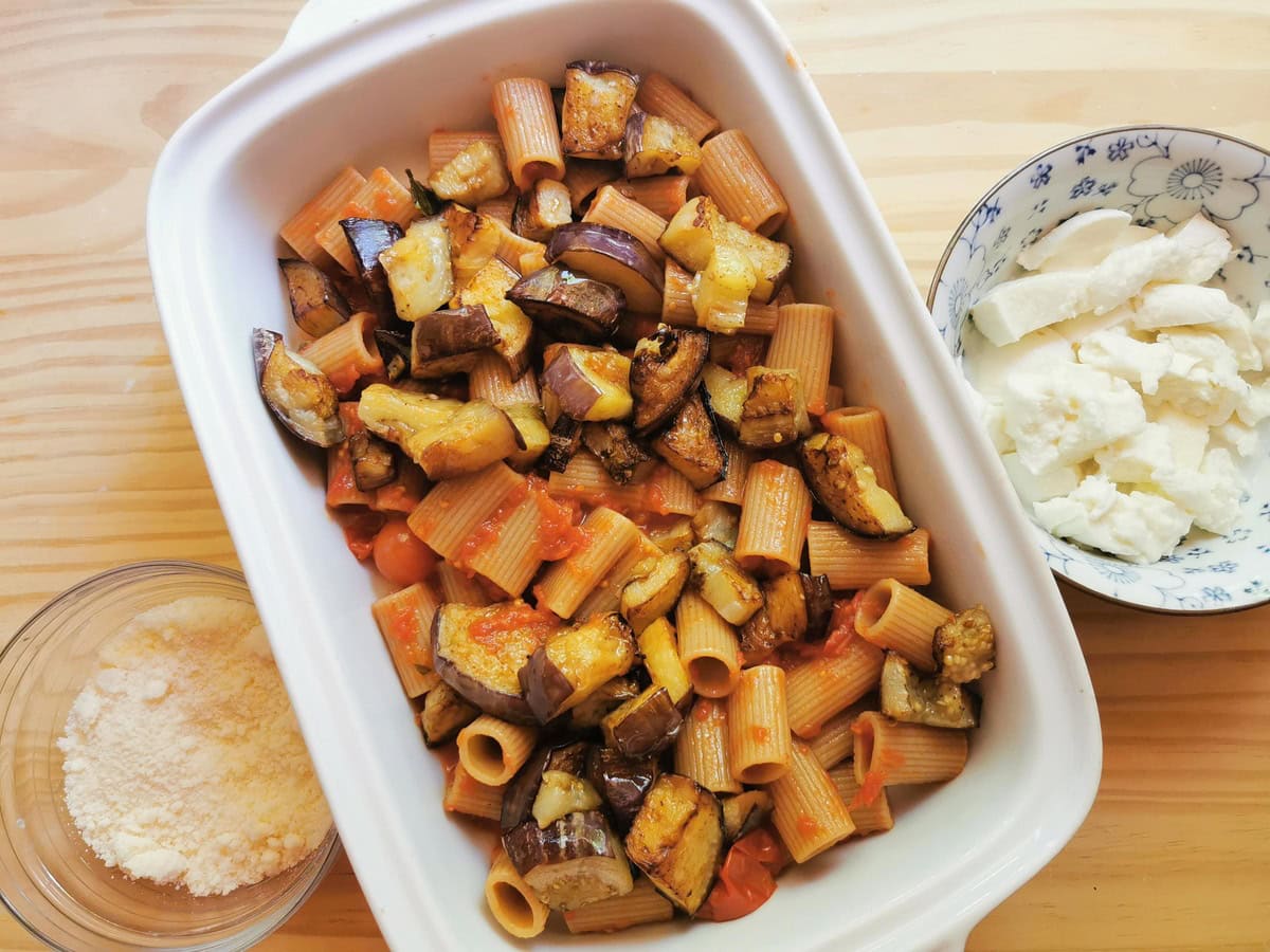 Whole wheat pasta with tomato sauce and eggplant cubes in white oven dish.