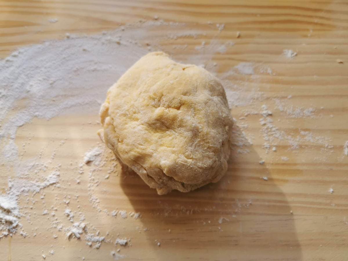 Unkneaded ravioli dough ball on wood surface.