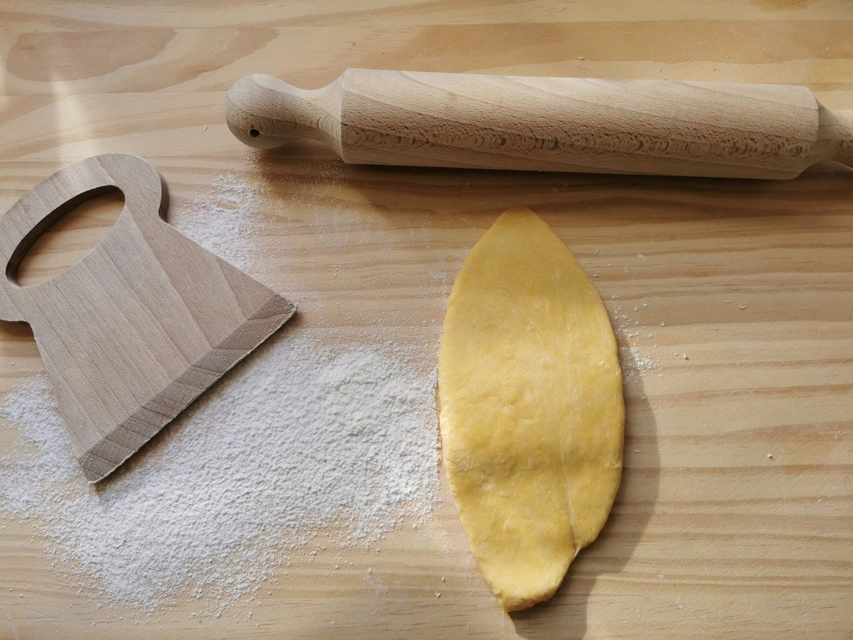 Piece of flatten egg pasta dough on wood surface with rolling pin.