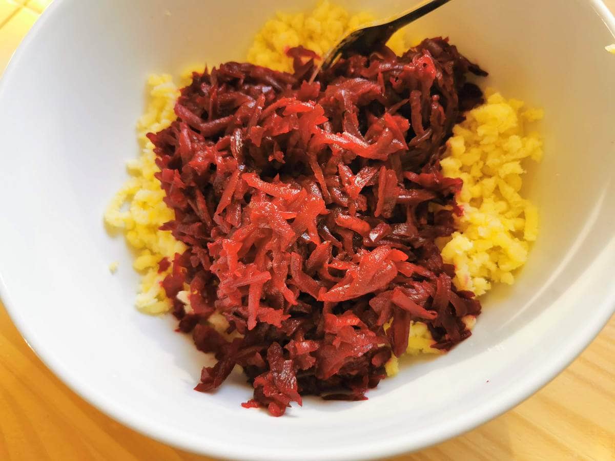 Grated beetroot with grated potato in white bowl.