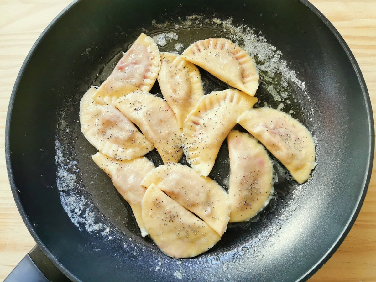 Cooked beetroot ravioli in pan with melted butter and poppy seeds.