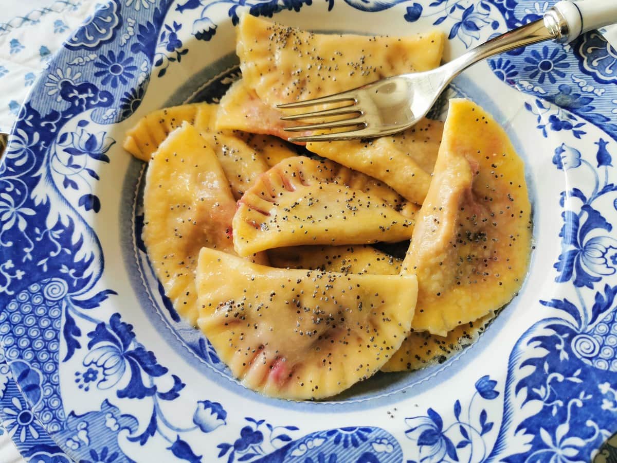 Beetroot and potato ravioli with poppy seeds in blue and white dish.