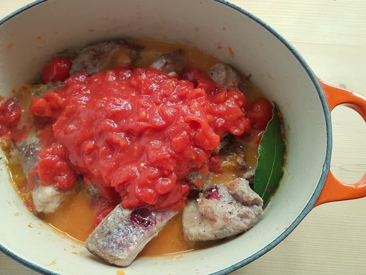 Pork ribs in Dutch oven with vegetables, tomato passata/pulp and bay leaf.