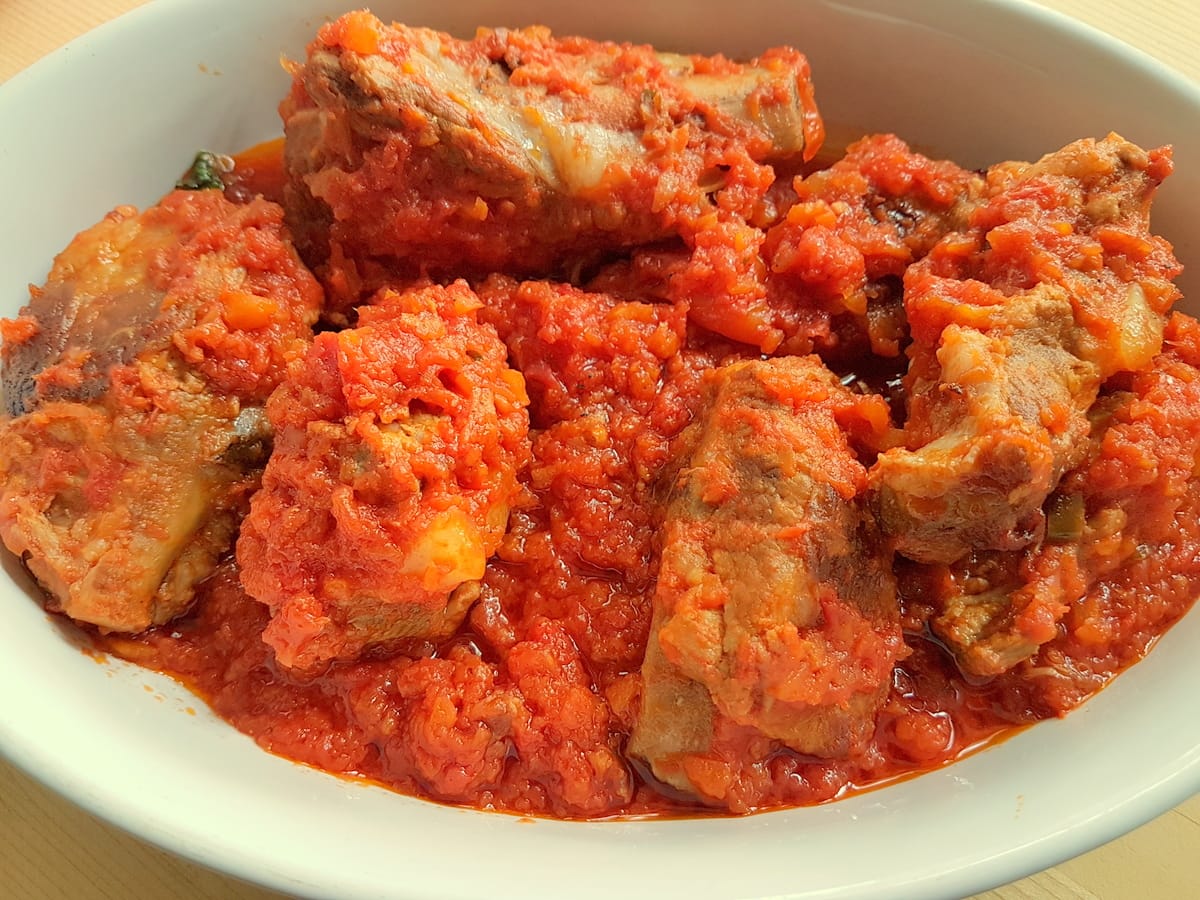 Italian braised pork ribs with tomato sauce in large oval white dish.