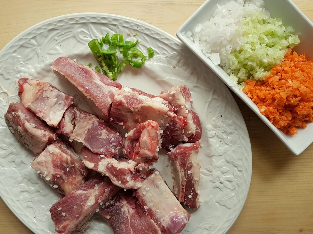 pork ribs rubbed with seasalt on white plate. Finely chopped onion, carrot and celery in white bowl.