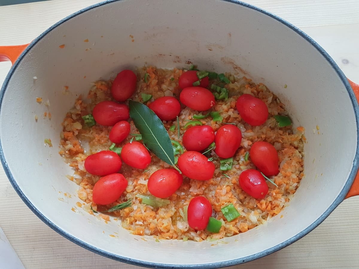 chopped onion, carrot and celery with small tomatoes and a bay leaf in Dutch oven.