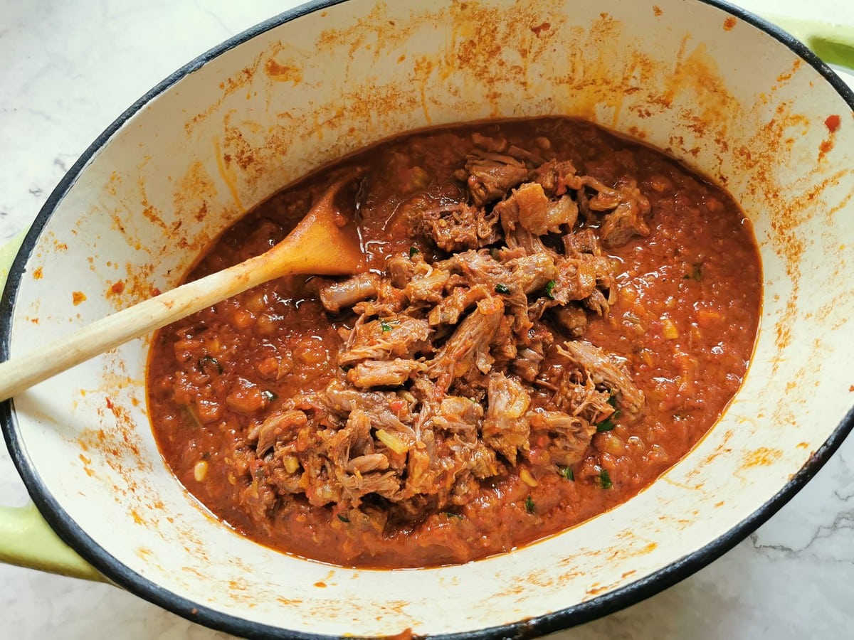 Shredded oxtail meat added to sauce in Dutch oven.