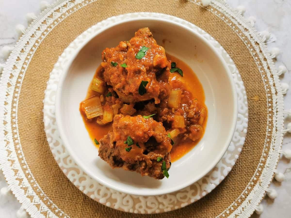 Whole pieces of oxtail with sauce in white bowl.