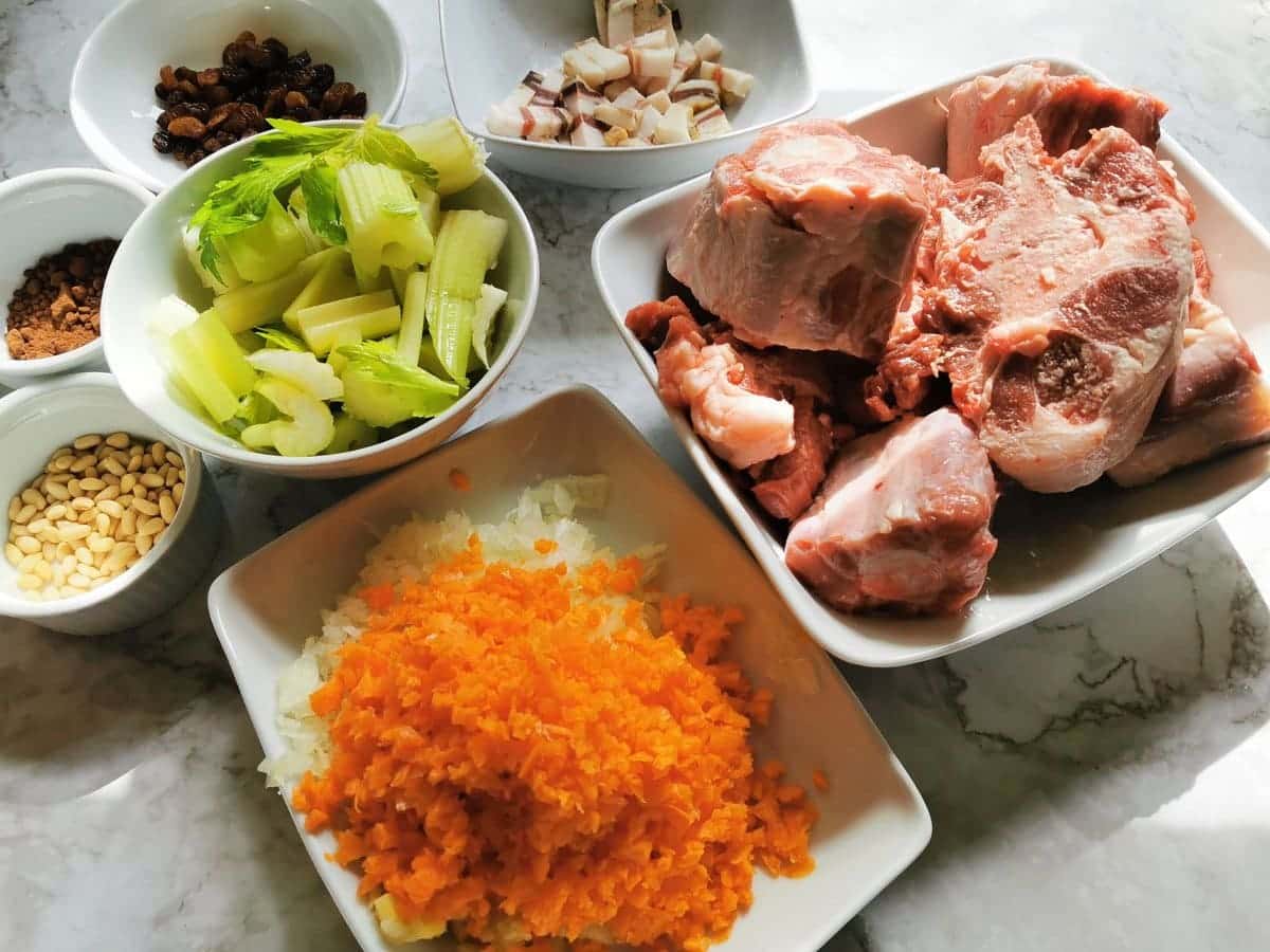 prepared oxtail ragu ingredients. Finely chopped onion, carrot and celery in white bowl. Washed oxtail pieces in white bowl and celery cut into larger pieces in white bowl.