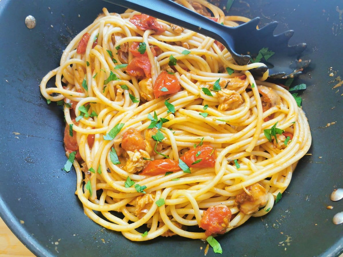 Bucatini mixed with braised rabbit ragu in deep skillet with fresh parsley sprinkled on top.