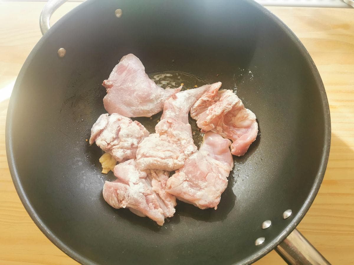 Floured rabbit pieces in deep skillet with garlic and chili flakes.