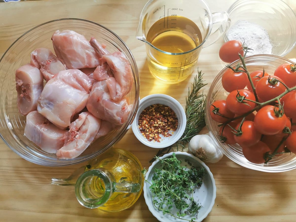 Ingredients for braised rabbit ragu: rabbit pieces, cherry tomatoes, garlic, white wine, flour, fresh rosemay and thyme and chili flakes.