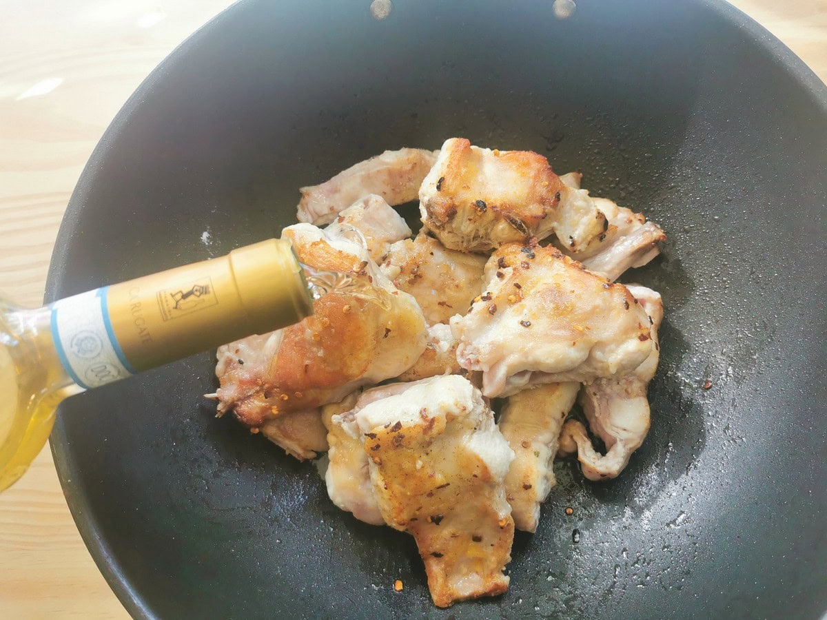 Browned rabbit pieces in deep skillet  with wine being added.