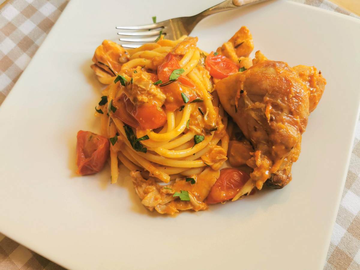 Bucatini pasta with braised rabbit ragu on white plate with whole rabbit piece on the side.