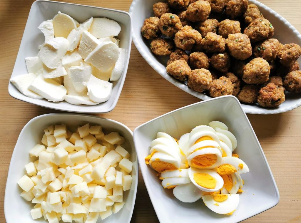 hard boiled eggs, cubed cheese and meatballs all in white bowls