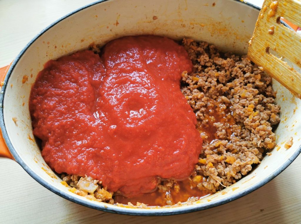 tomato passata added to meat sauce in Dutch oven