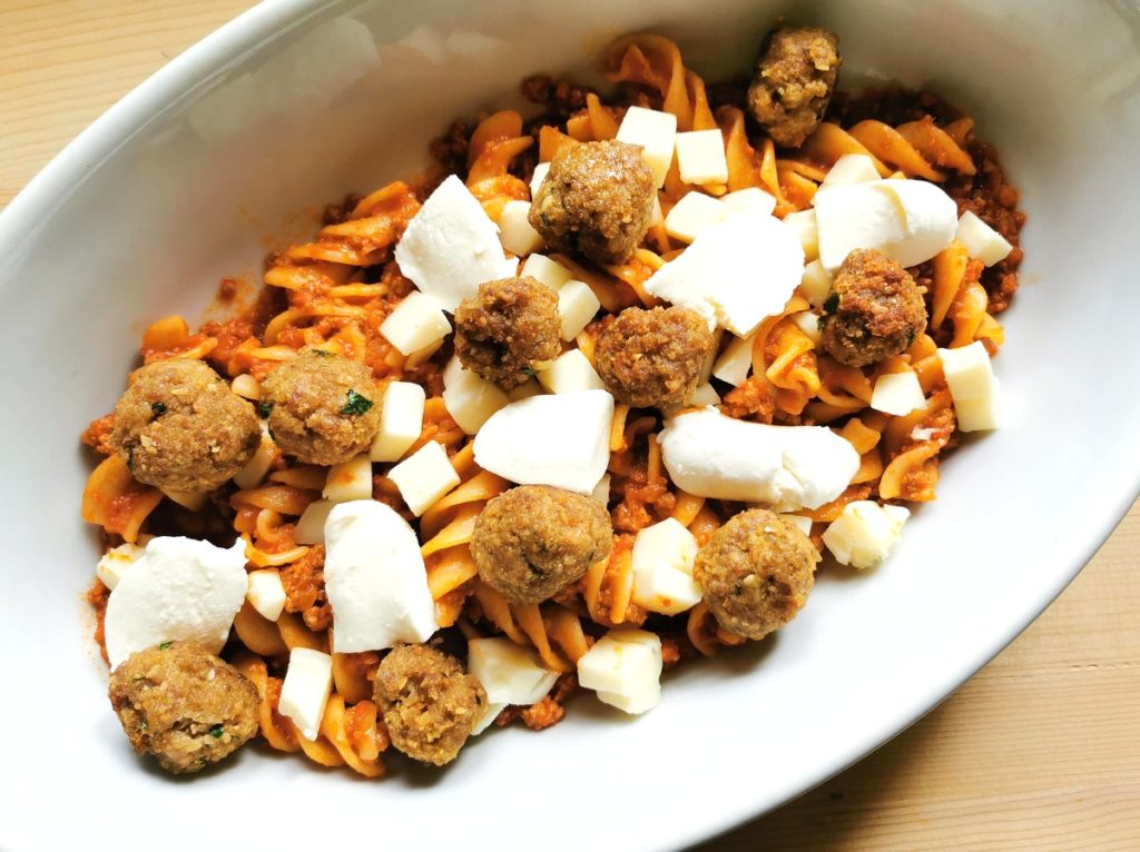 meatballs and cubed cheese scattered over pasta and ragu in oven dish