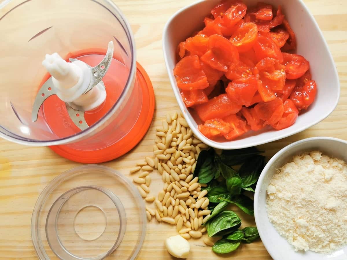 chopped peeled tomatoes in white bowl, grated Parmigiana in white bowl and pine nuts, basil leaves and garlic.