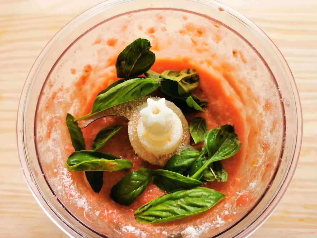 Basil leaves in food processor on top of tomato sauce.