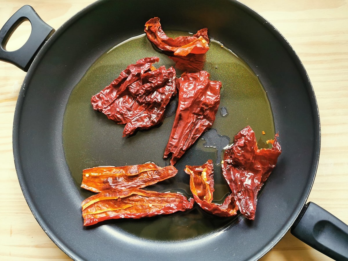 Senise peppers being cooked in a pan with olive oil.