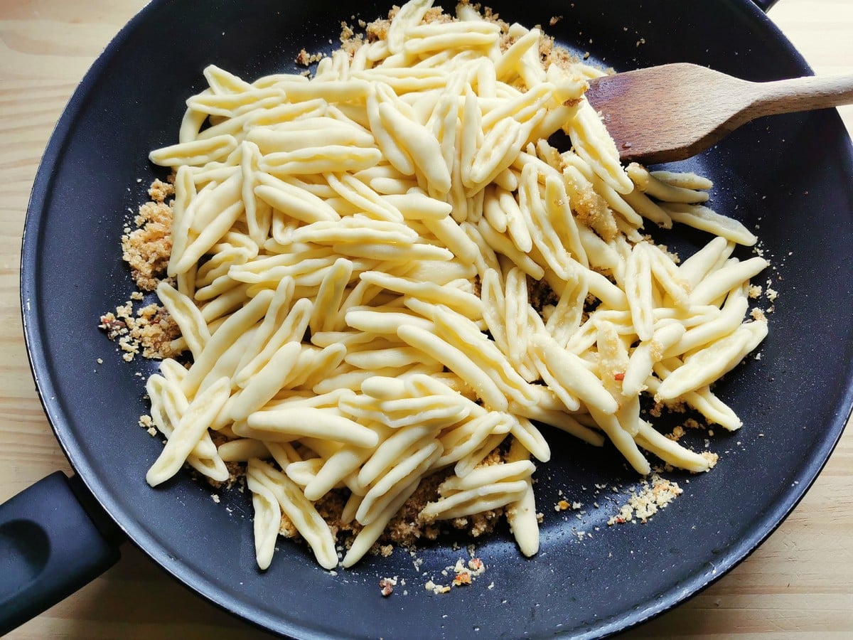 Pasta being mixed into the breadcrumbs.