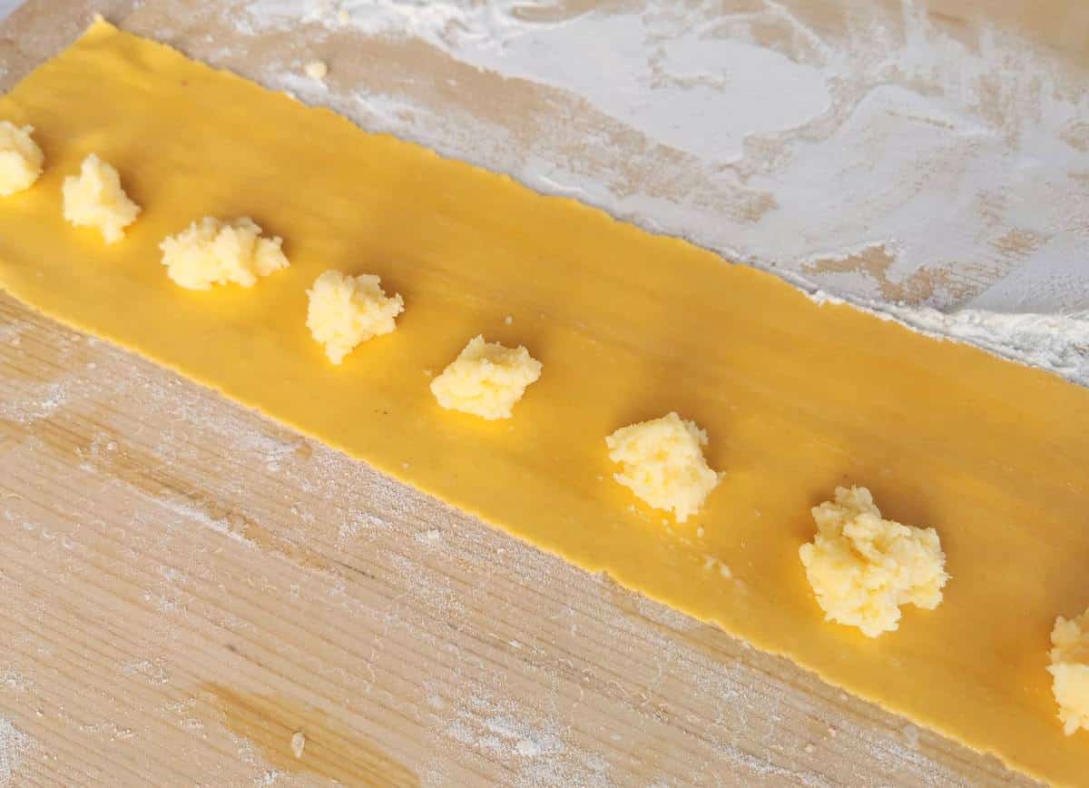 rectangular sheet of pasta dough with small mounds of cheese filling in a row along one side.