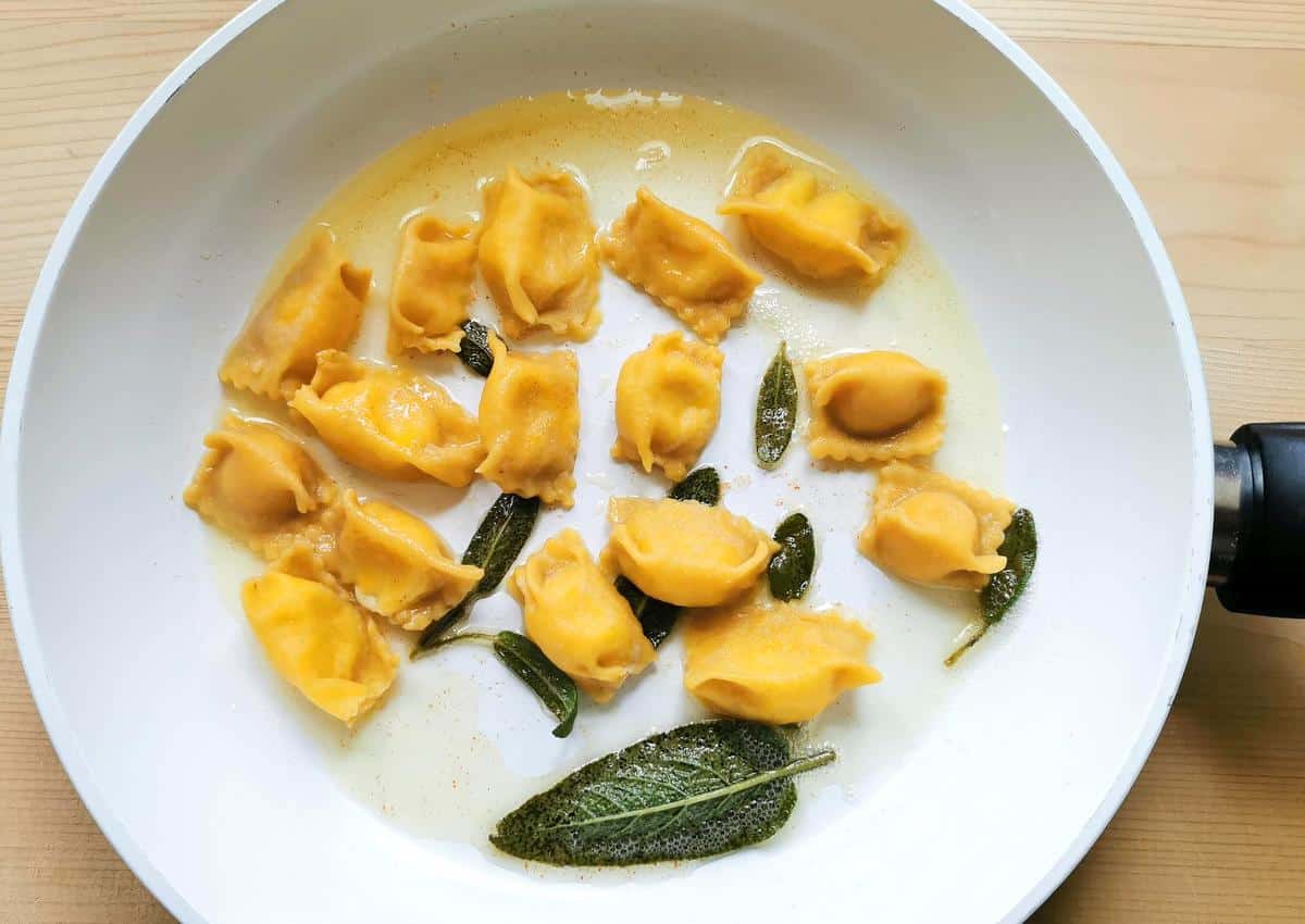 Cooked cheese stuffed agnolotti del plin in pan with melted butter and sage.