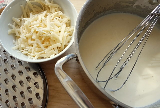 grated fontina cheese in bowl and béchamel sauce in pan