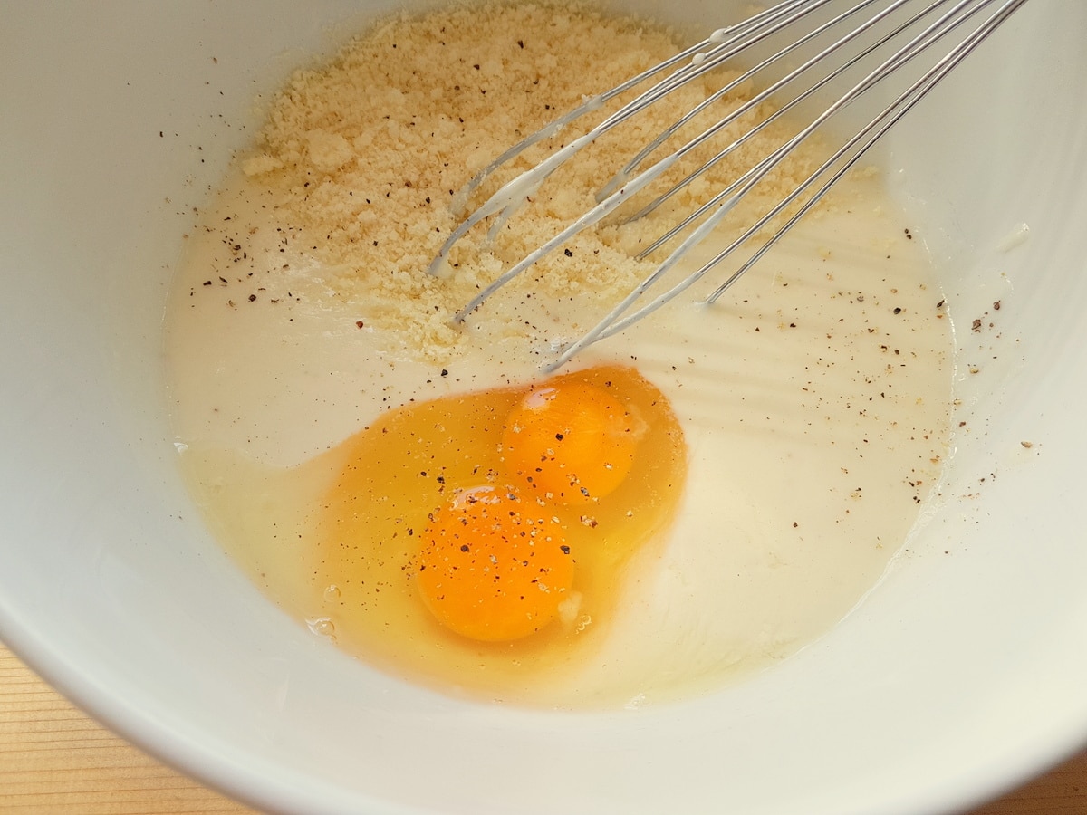 Ready béchamel sauce in white bowl with two eggs and grated grana.