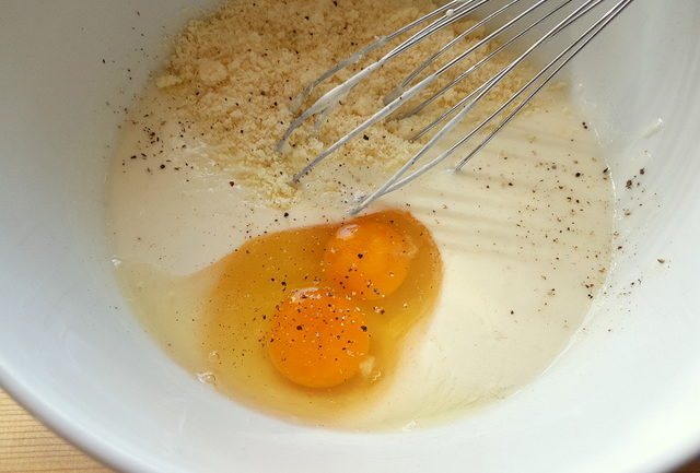 eggs, grated grana, béchamel, pepper and salt in white mixing bowl with whisk